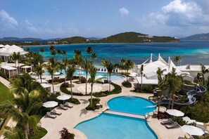 Un resort con una piscina grande, palmeras y vistas al océano.