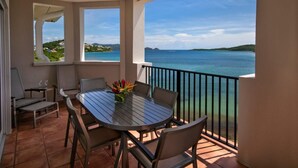 Ein Balkon mit Tisch und Stühlen, der Blick auf ein klares blaues Meer und entfernte Landstriche freigibt.
