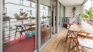 Een modern balkon met houten vloer, glazen deuren en uitzicht op omliggende gebouwen.
