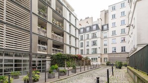 Een geplaveid straatje omzoomd door moderne gebouwen met balkons, bloempotten en een heldere lucht.