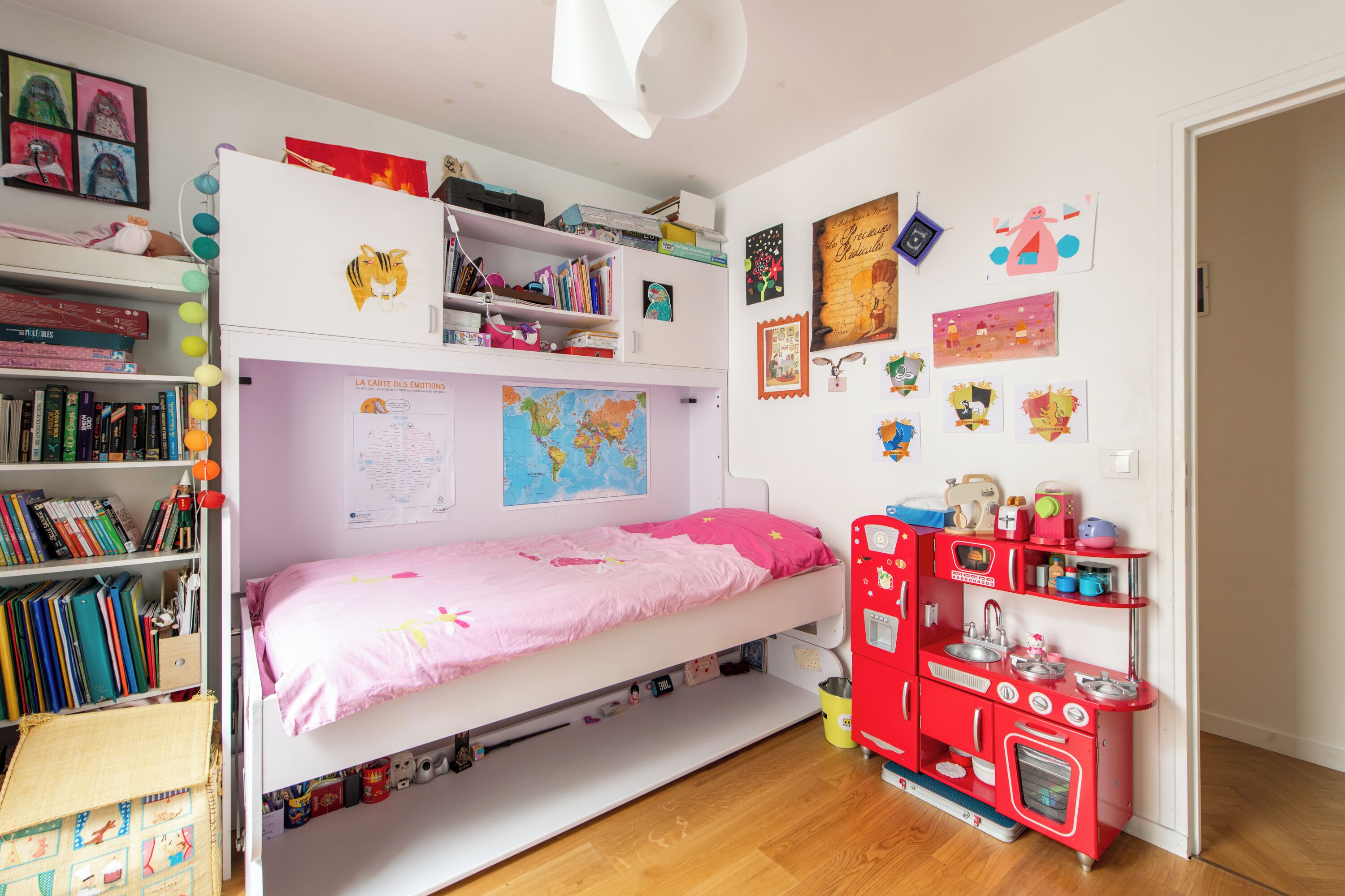 A child's bedroom with bunk beds, a bookshelf, a world map, and a play kitchen.