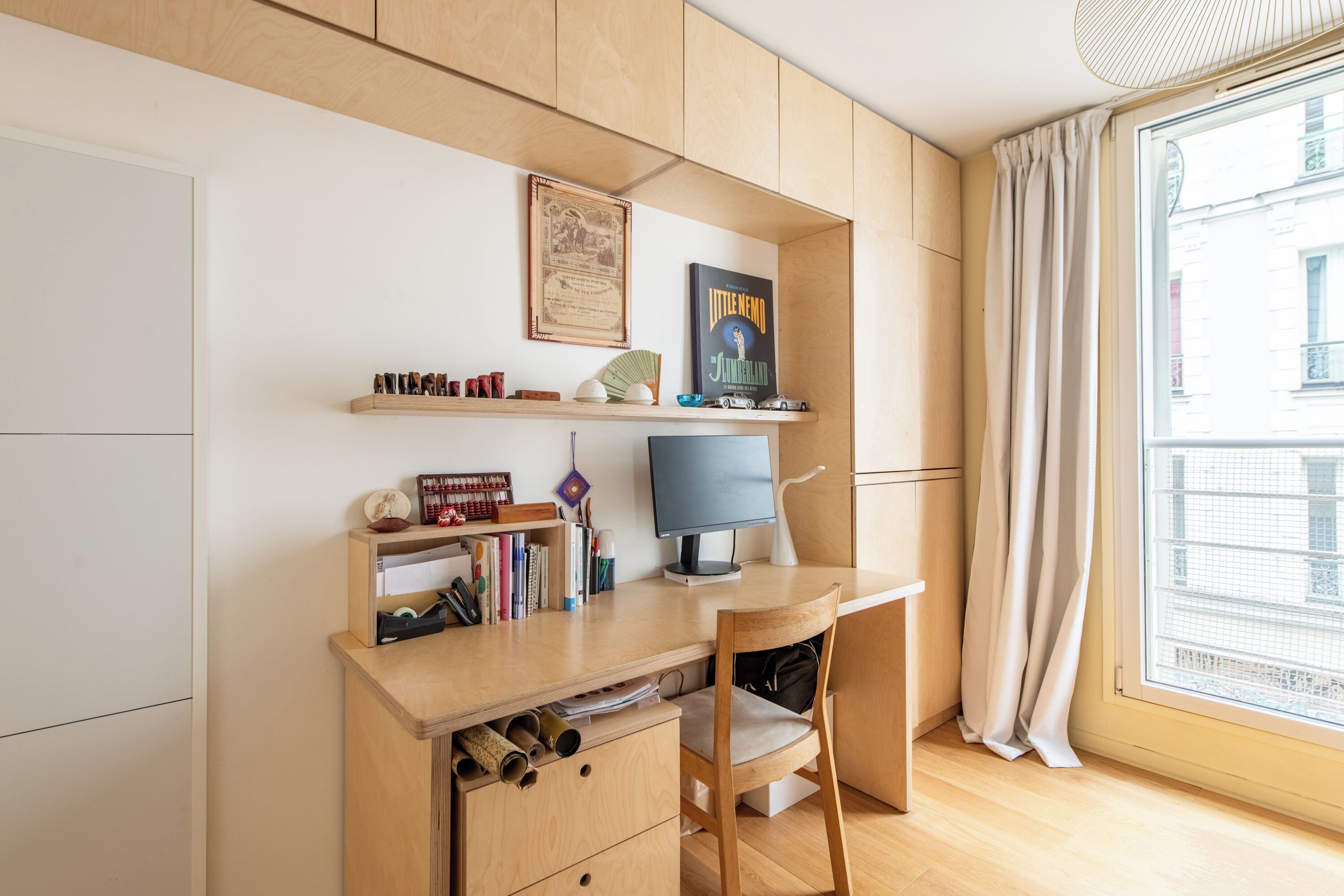 A modern, well-lit room with a wooden desk, a computer, and shelves with books and decorative items.