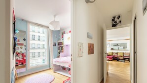 Een lichte kamer met een groot raam, een roze bed en een rode kinderkookset.