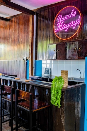 A rustic kitchen with wooden walls, a neon sign reading "Rancho Mayayí", and a small hanging plant.