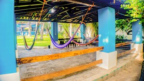 Un espacio al aire libre techado con piso de ladrillo, escalones de madera y coloridos hamacas colgando del techo.