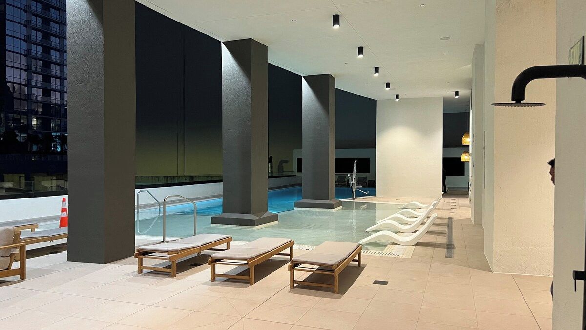 A rooftop pool area with lounge chairs and a view of a cityscape at night.