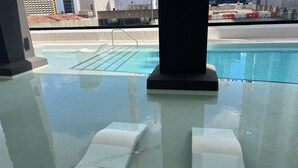 Krystalklart udsyn til en swimmingpool med glasbund, omgivet af et bassin med gelænder.
