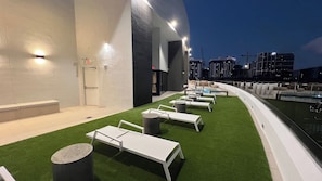 Un espace de détente extérieur avec des chaises longues blanches et une piscine, le tout entouré d’un bâtiment blanc à la façade incurvée.