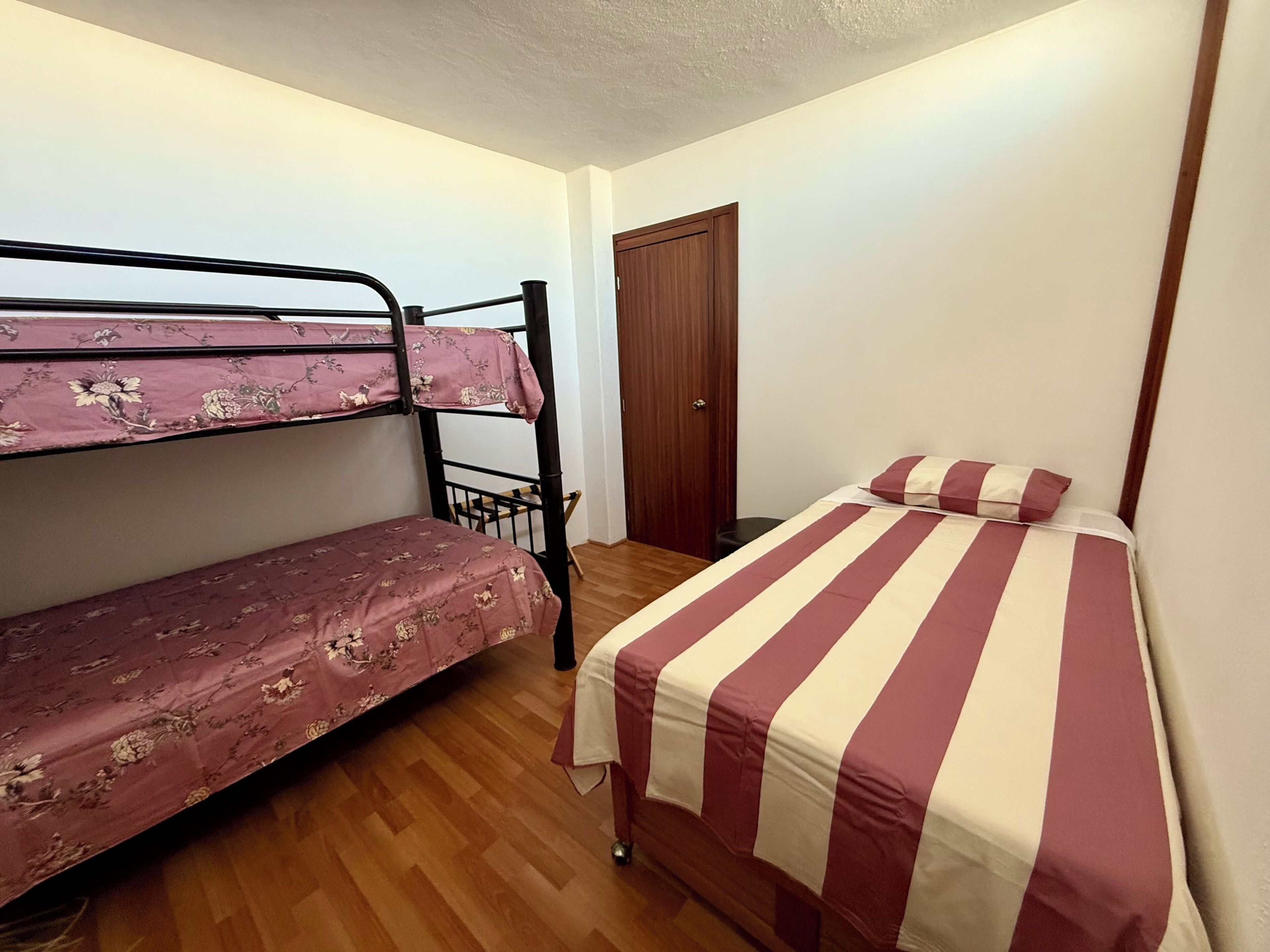 A room with a bunk bed and a single bed, wooden flooring, and a door.