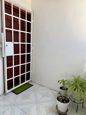 Une porte en bois fermée, dotée d’un cadre blanc, un sol carrelé et des plantes en pot près de la porte.