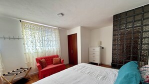 A bedroom with a bed, a red sofa, a wardrobe, and a window with curtains.