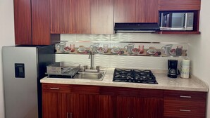 A kitchen with wooden cabinets, a stainless steel refrigerator, a microwave, a gas stove, and a sink.