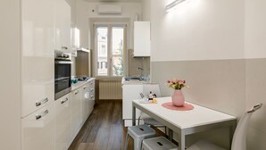 Een moderne keuken met witte kasten, een inbouwoven en een raam met uitzicht op gebouwen.