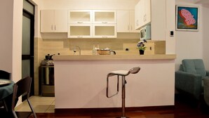 A compact kitchen with white cabinets, a central island with a bar stool, a microwave, and a small oven. - 1 bedroom comfort apartment in Cusco (Cusco)