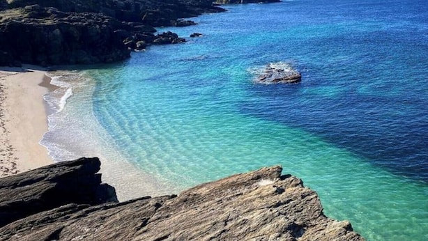 Et kystlandskab med klart, blåt vand, en sandstrand og klippeformationer.