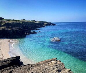 Un paisaje costero con aguas azul cristalino, una playa de arena y afloramientos rocosos.