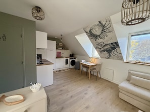 Un dormitorio tipo loft moderno con techo inclinado, comedor, cocina y un amplio ventanal con vistas a la ciudad.