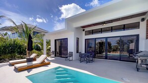 Ett modernt hus med en swimmingpool, utomhusmöbler och utsikt över poolen.