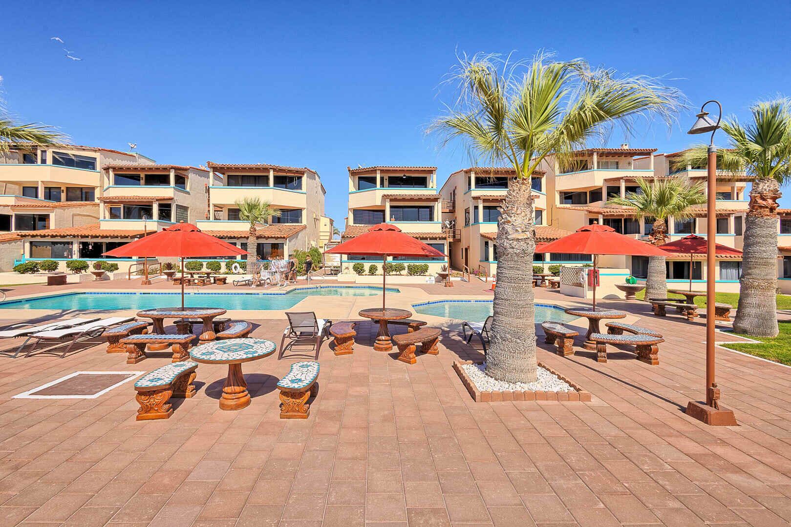 A resort with a swimming pool, outdoor seating, and palm trees.