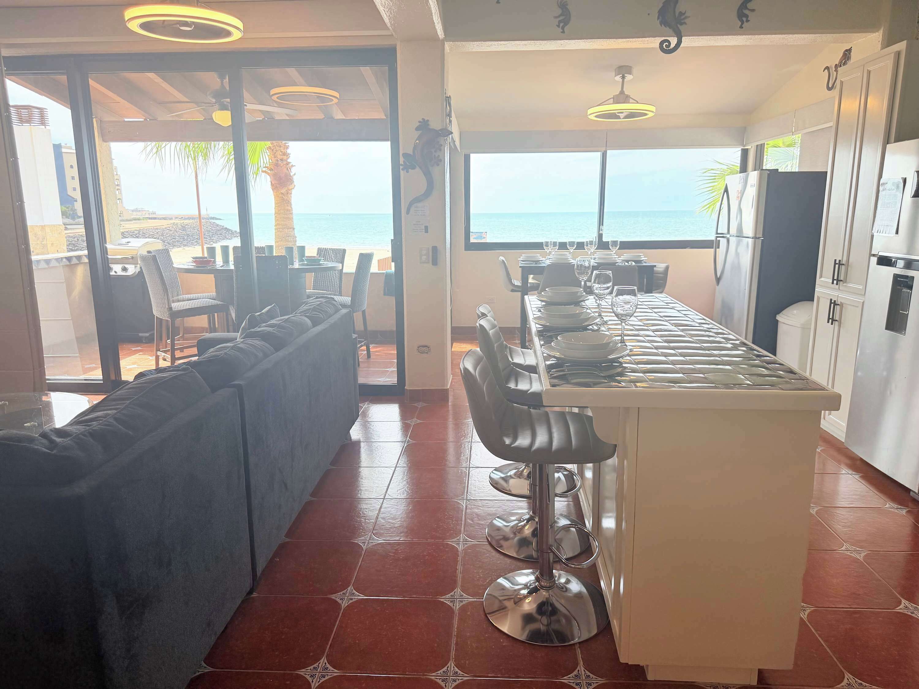 Una cocina moderna con barra, ventanas amplias con vistas al mar y un comedor con sofá y sillas.