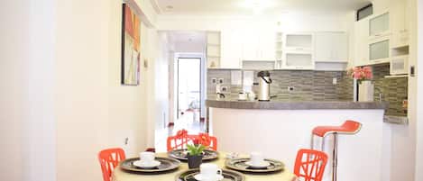 A dining area with a round table set for four, surrounded by red chairs, and a kitchen area with white cabinets and a microwave.
