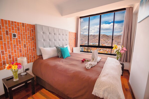 Een hotelkamer met een groot bed, uitzicht op een stadsbeeld en een muur met een bakstenen patroon.