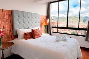 Hotelkamer met een groot bed, een bakstenen muur en uitzicht op een stadsbeeld door een raam.