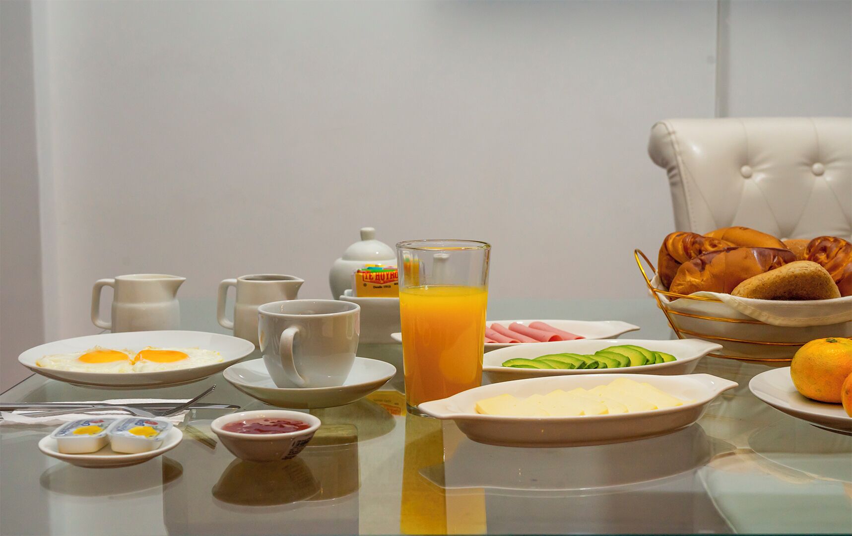 A breakfast setting with plates of eggs, toast, and fruit, along with a glass of orange juice.