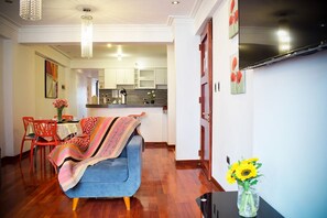 Een moderne woonkamer met een blauwe bank, een eethoek met rode stoelen en een keuken op de achtergrond.