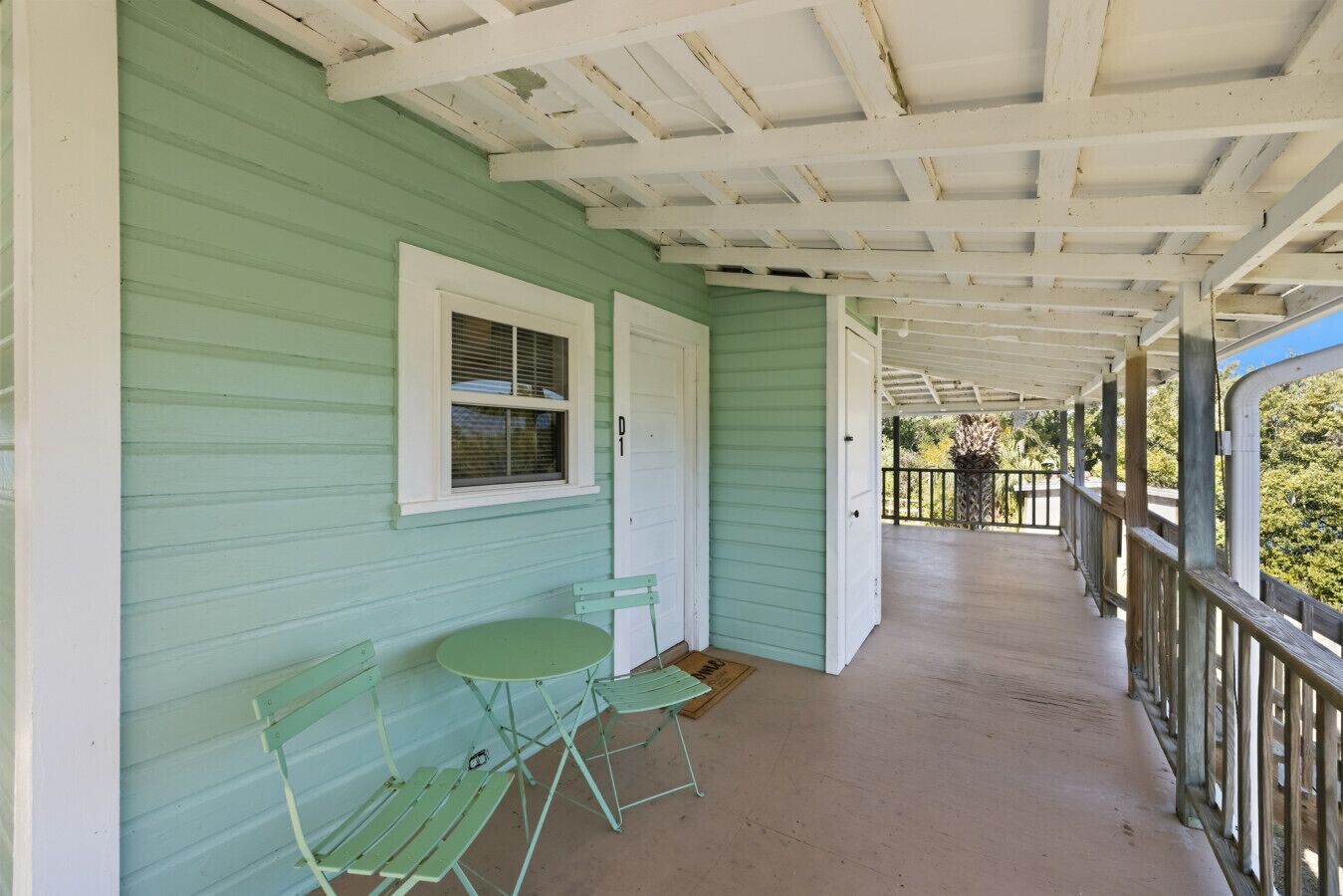 A covered porch with a green exterior, white trim, and a small table with chairs.