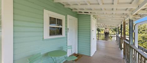 A covered porch with a green exterior, white trim, and a small table with chairs.