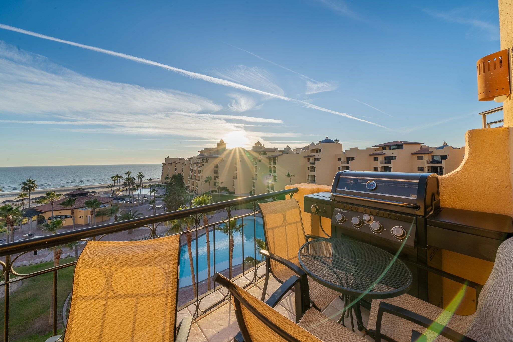 A balcony with a grill, a pool, and a view of the ocean and buildings.