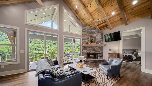 Amplia sala de estar con chimenea, ventanas grandes y balcón con vista al bosque.
