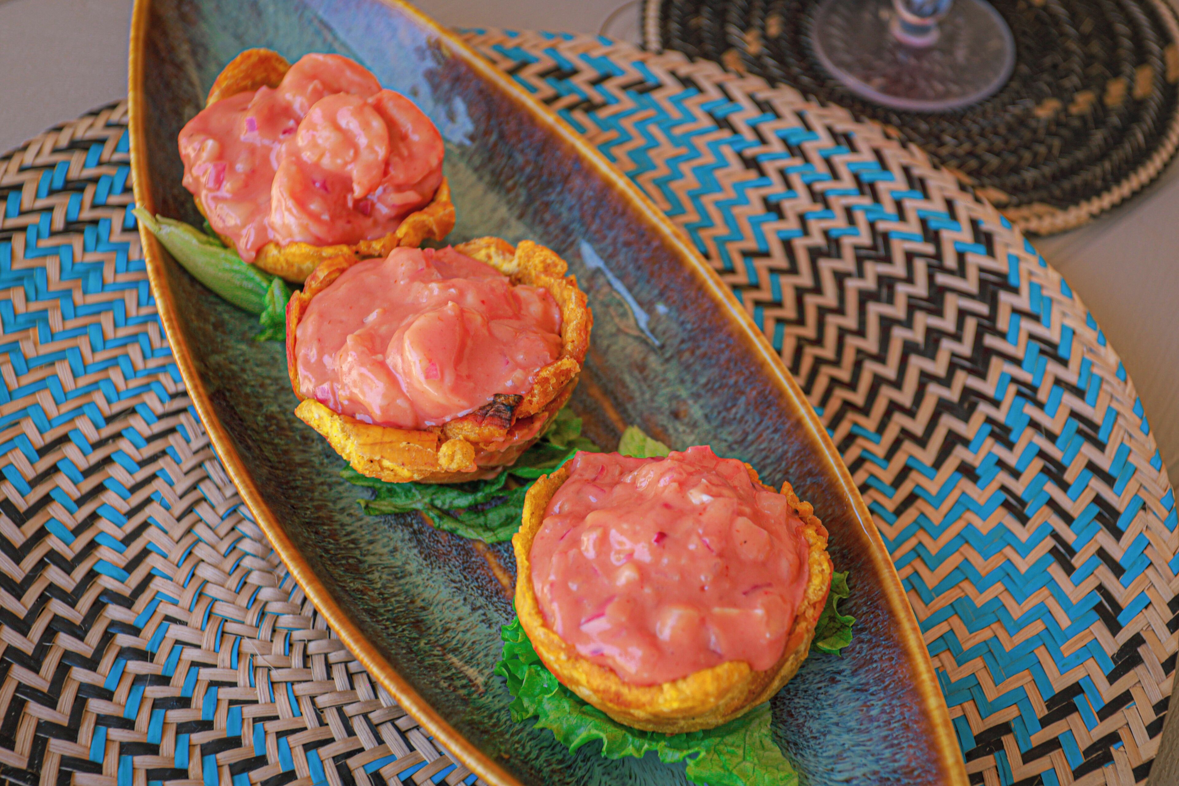Un plato con tres sándwiches abiertos sobre un camino de mesa tejido.