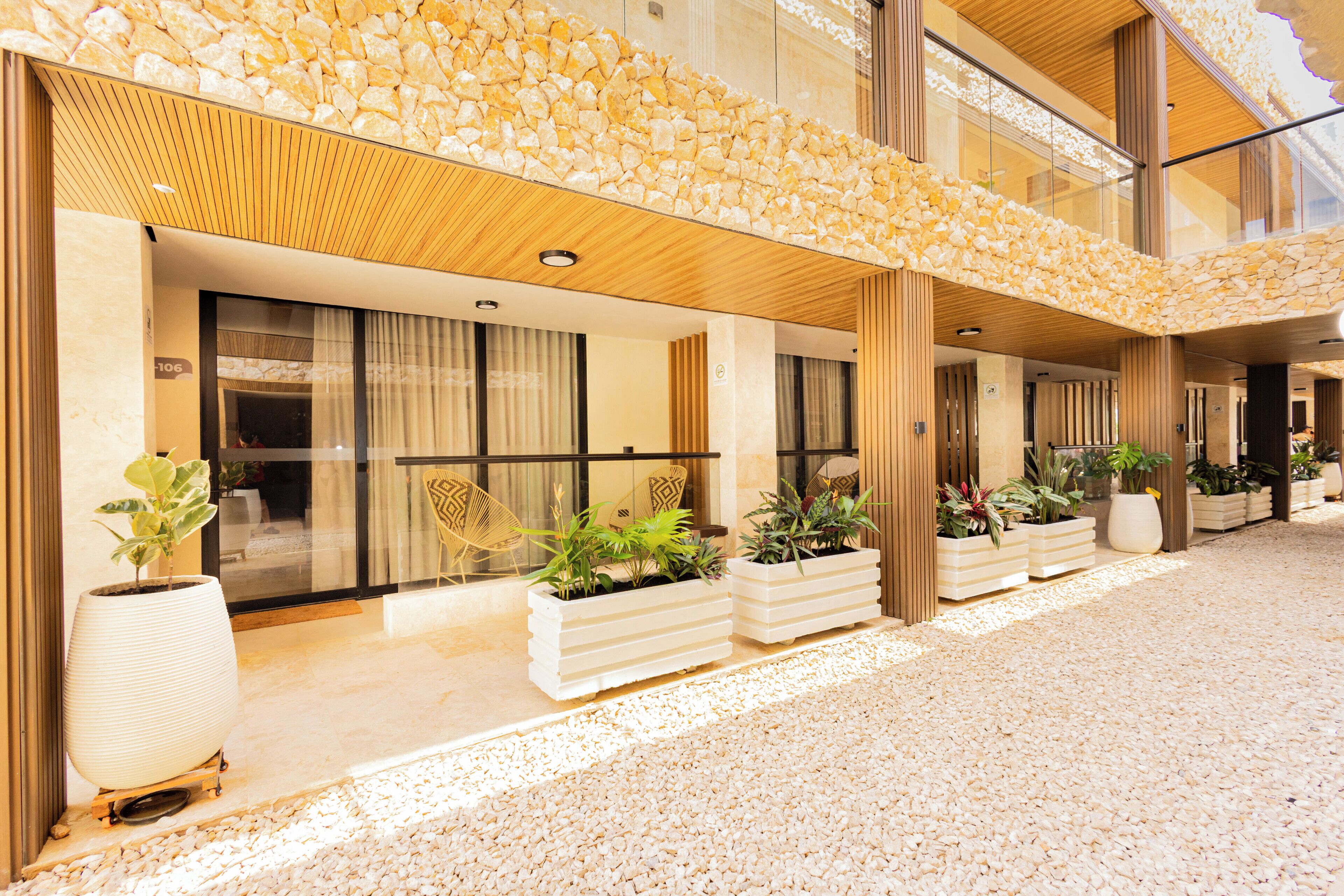 Fachada de hotel de piedra, con amplias ventanas y macetas con plantas.