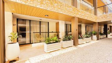 Fachada de hotel de piedra, con amplias ventanas y macetas con plantas.