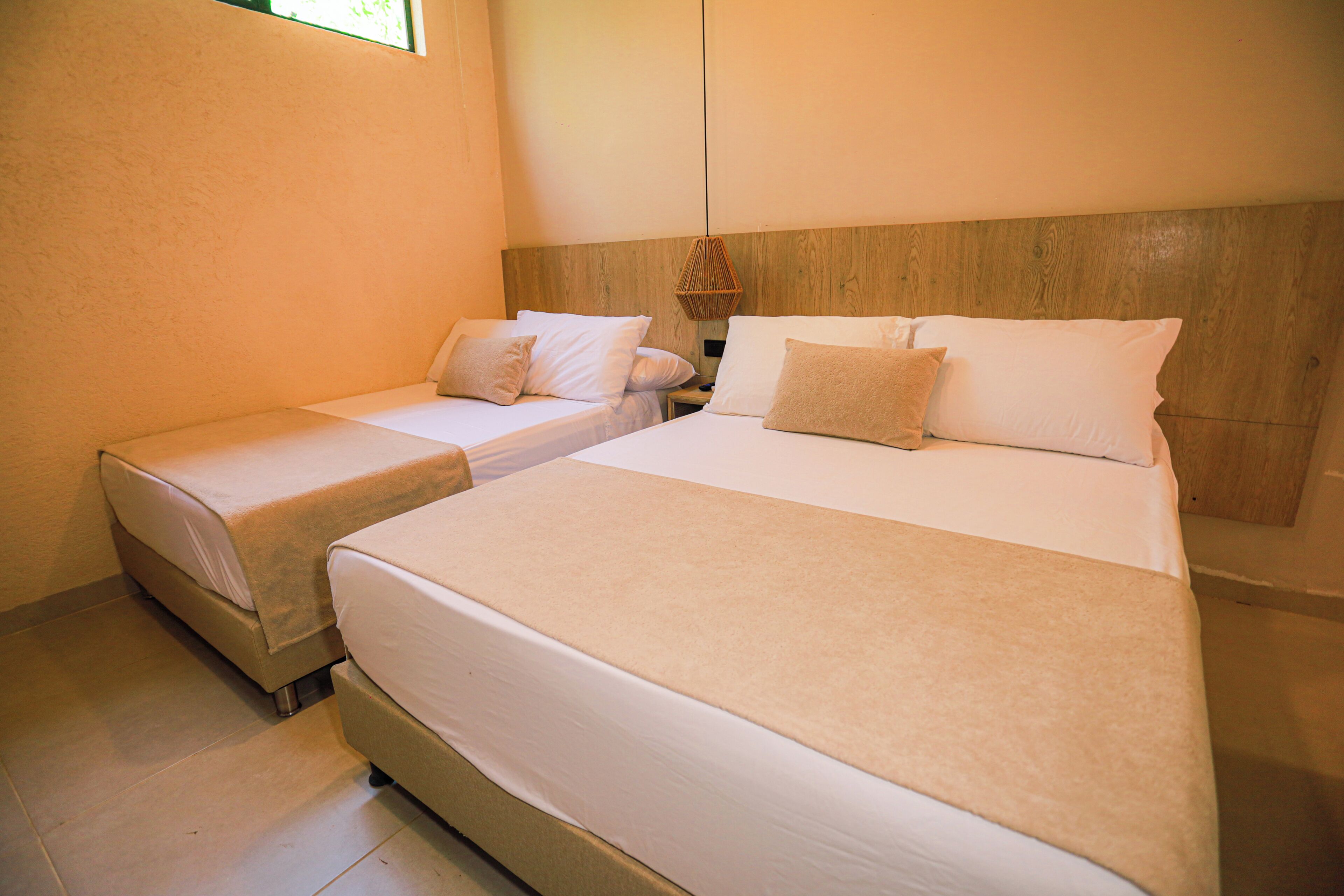 Ein Hotelzimmer mit zwei Betten, einem Holzkopfteil und einer Hängelampe.