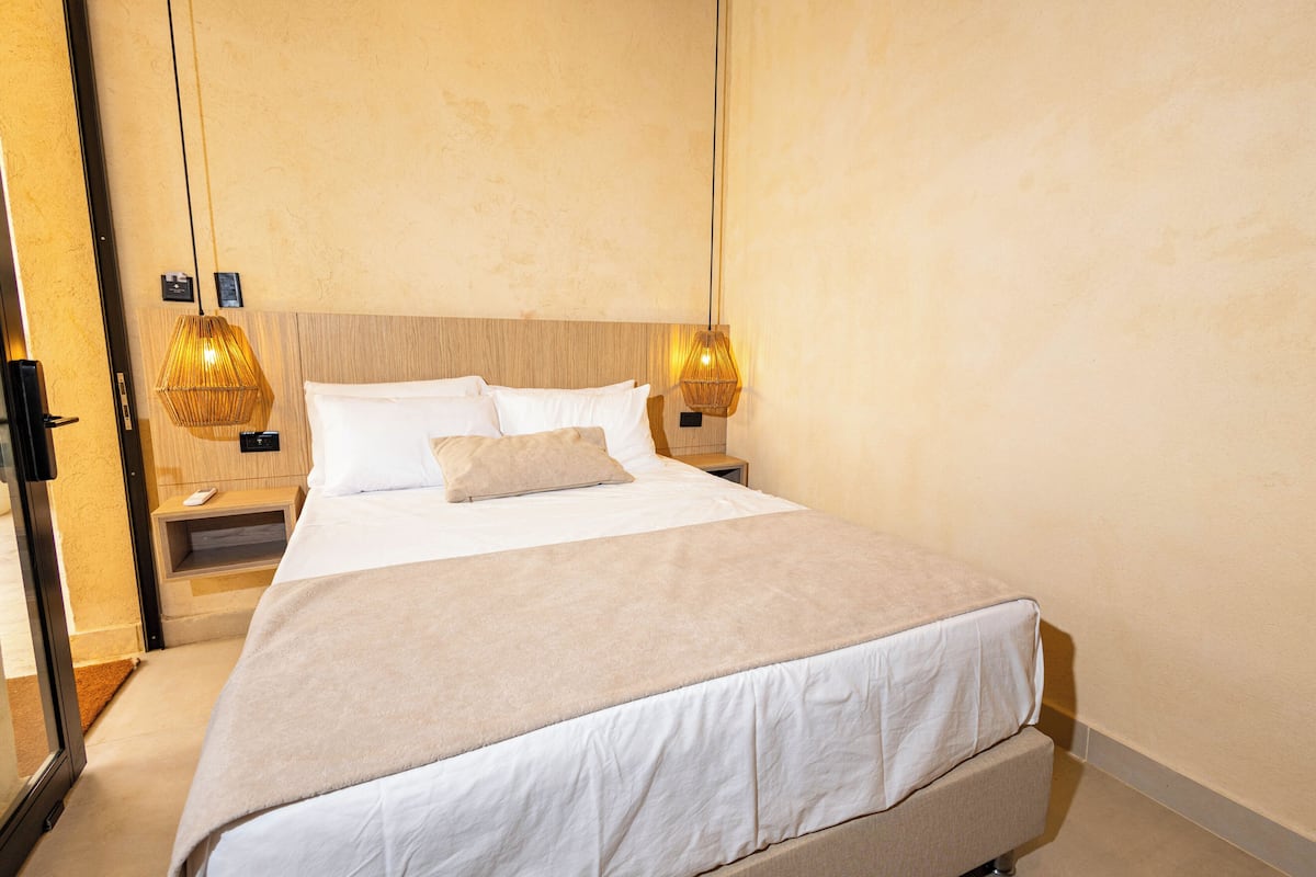Una habitación de hotel con una cama grande, mesitas de noche y dos lámparas fijadas a la pared.