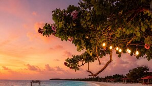A beachside table set with chairs, a lantern, and a view of the ocean at sunset. - Handhuvaru Maldives (Milandhoo)