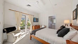 A hotel room with a bed, a chair, a desk, a TV, and a bathroom visible through an open door. - Brokenback Homestead (Pokolbin)