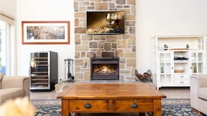 A living room with a stone fireplace, a wooden coffee table, a white cabinet, and a framed picture on the wall. - Brokenback Homestead (Pokolbin)