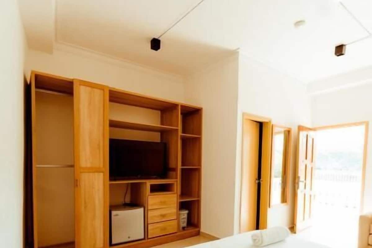 A bedroom with a large bed, wooden wardrobe, and a television.