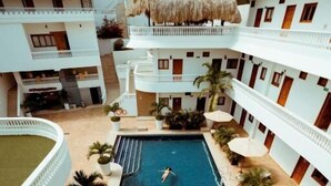 Et hotel i flere etager med en central swimmingpool, udendørs siddepladser og en bindingsværksbygning.