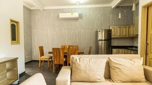 En kompakt opholdsstue med sofa, spisebord, stole og et tekøkken.