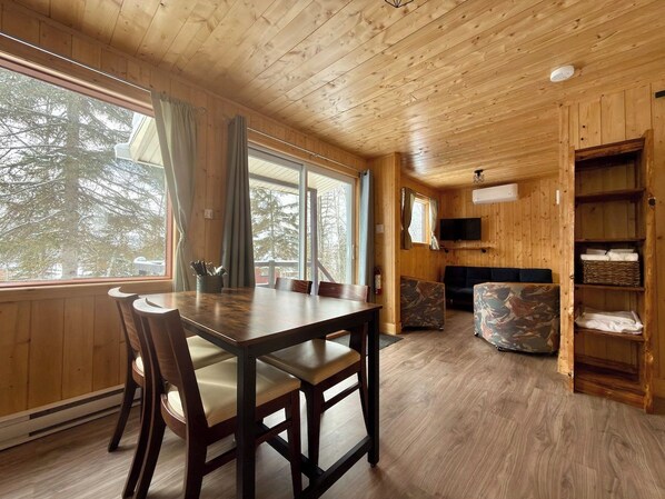A wooden interior with a dining table, chairs, a sofa, and a bookshelf.