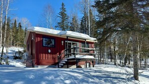 Una cabaña roja con balcón, rodeada de nieve y árboles.