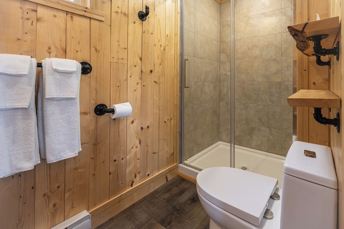 Une salle de bain avec un lambris en bois, des toilettes, un espace douche et un porte-serviettes avec des serviettes.