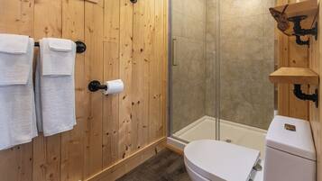 Une salle de bain avec un lambris en bois, des toilettes, un espace douche et un porte-serviettes avec des serviettes.