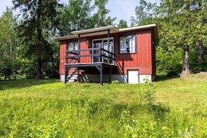A red cabin with a balcony, surrounded by a grassy field and trees.