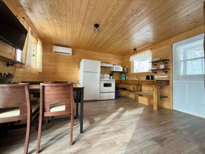 Eine Küche mit Holzwänden, einem Essbereich, inklusive Tisch und Stühlen, einem Kühlschrank und einem Herd.